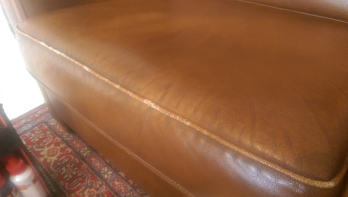 Voor: Cognackleurige leren bank met een versleten, verkleurde biesrand die is bijgekleurd, waarna de zitting weer een egale, warme kleur heeft